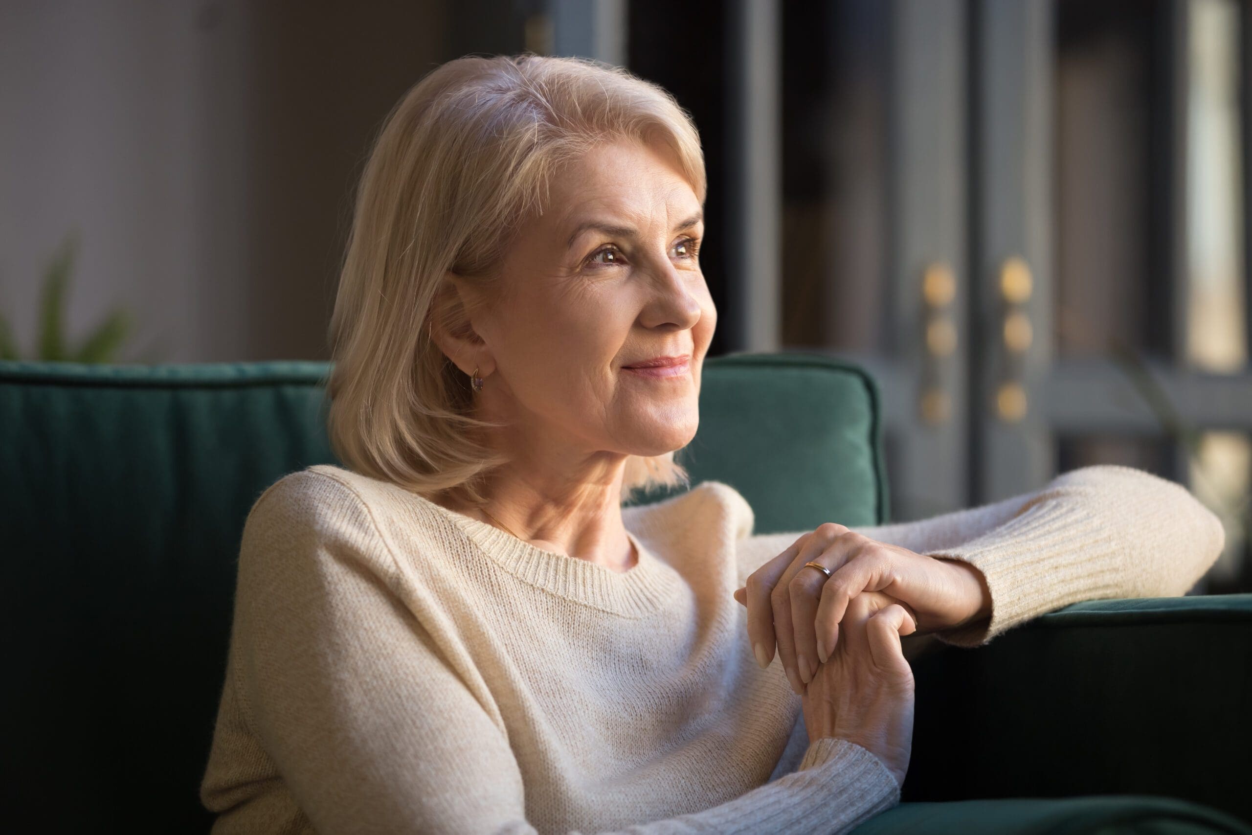 Thoughtful elderly woman gazing out a window in soft natural light.