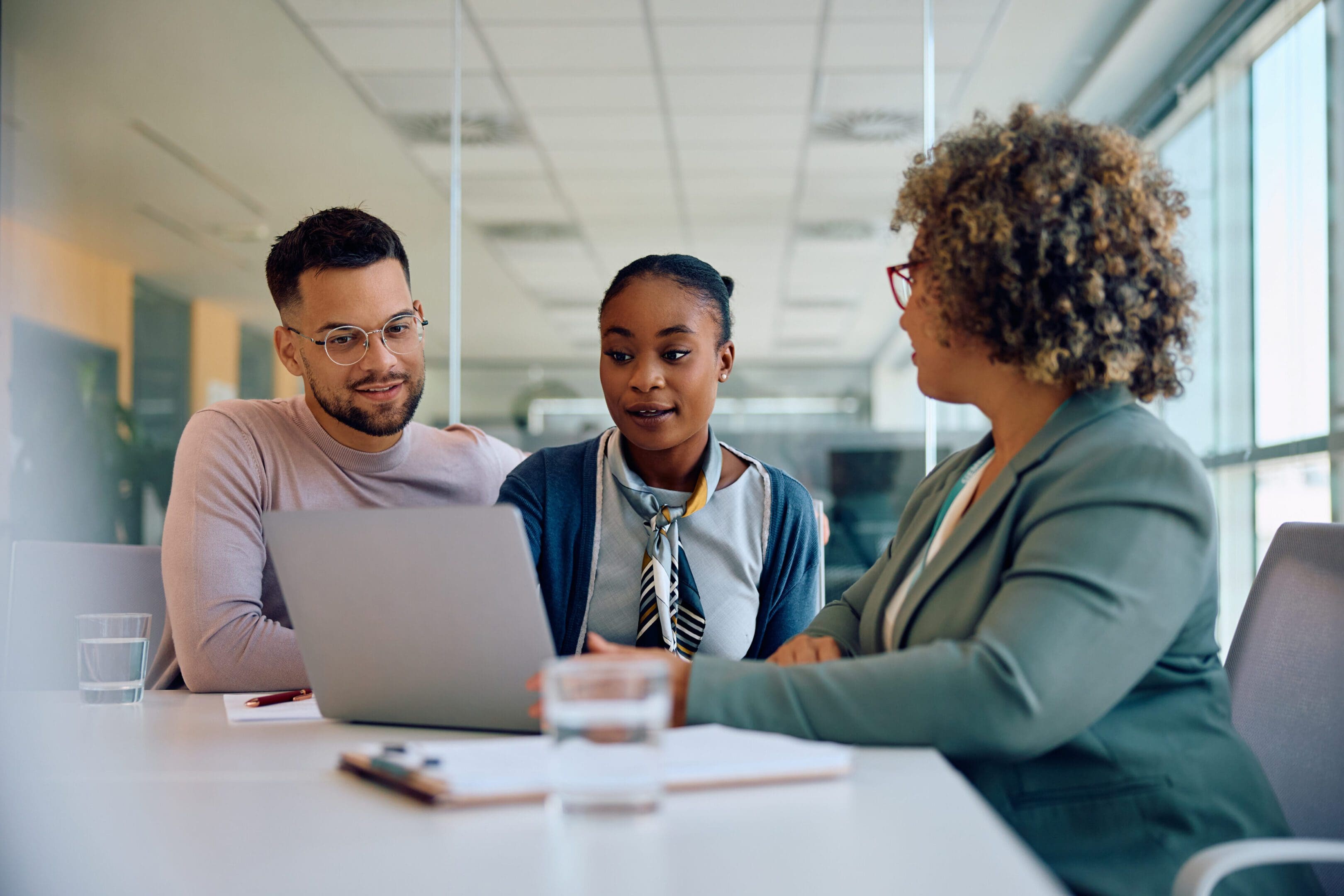 Three professionals discussing work around a laptop in an office.